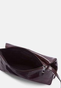 Pochette in ecopelle bordeaux con texture liscia, chiusura a zip e tasca interna; forma rettangolare piatta con manico laterale.