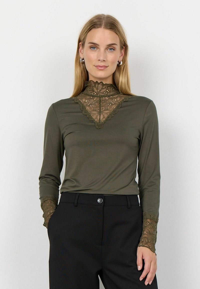 Maglia a maniche lunghe verde oliva con un alto colletto in pizzo e dettagli in pizzo alle maniche, abbinata a pantaloni neri a vita alta.