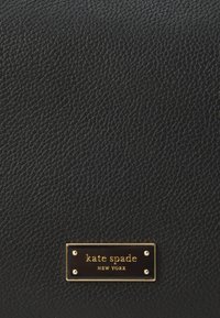 Fekete textúrázott bőr pénztárca arany logólemezzel, amelyen a "kate spade NEW YORK" márkaneve szerepel, valamint négy arany szegeccsel.