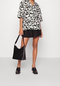 Camicia a maniche corte bianca e nera con motivo ondulato, abbinata a una gonna nera e una borsa hobo nera con tracolla testurizzata e scarpe nere a punta quadrata.