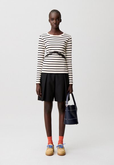 Top de manga larga a rayas en colores negro y crema, pantalones cortos negros, calcetas naranjas y zapatos beige con cordones azules. Lleva un bolso azul marino.