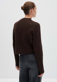 Woman with hair in bun wearing a dark brown cropped sweater and faded black jeans, shown from the back against a plain background.