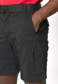 Black shorts made of lightweight, stretch fabric with a side zip pocket, belt loops, and deep hand pockets; features smooth texture and tailored fit.