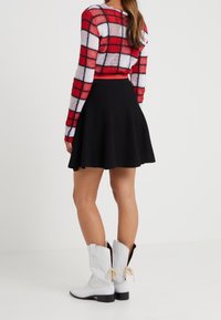 Red and white plaid sweater with long sleeves, paired with a black flared skirt and white leather cowboy boots with a low heel.