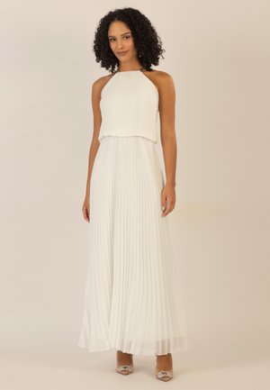 Witte geplooide maxi-jurk met een halternek, vloeiende stof en een gelaagd ontwerp, aangevuld met sprankelende hakken.