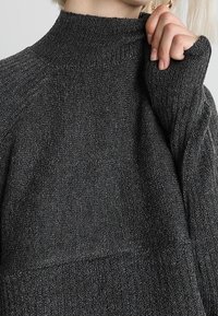 Ciemnoszary sweter z golfem o prążkowanej fakturze i mankietach, cechujący się luźnym krojem i gładkim dzianinowym materiałem.