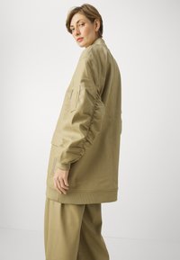 Khaki oversize bunda s nariasenými rukávmi, rebrovanými manžetami a prednou vreckom. Hladká tkanina s minimalistickým dizajnom.