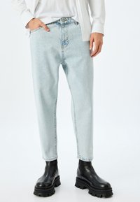 Pantalones vaqueros rectos de color azul claro, hechos de tela de denim, con un efecto desvaído y diseño de cinco bolsillos, combinados con botas negras de tobillo grueso.
