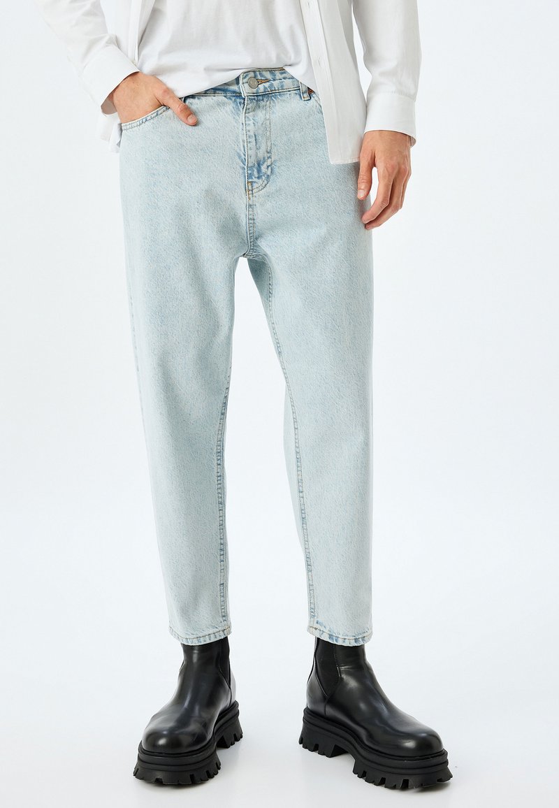 Pantalones vaqueros rectos de color azul claro, hechos de tela de denim, con un efecto desvaído y diseño de cinco bolsillos, combinados con botas negras de tobillo grueso.