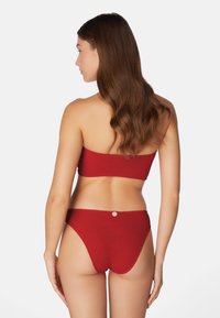Röd ribbad bikiniuppsättning med ett strapless-top och högskuren botten. Noterbar knappdetalj på baksidan av botten. Slät textur.