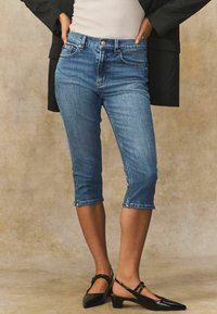 Denim capri jeans i mellanblått med en åtsittande design, medelhög midja och uppvikt nederkant. I kombination med svarta slingback med klack.