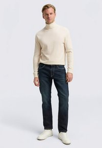 Light beige turtleneck sweater with ribbed texture, paired with dark blue jeans and white sneakers. Simple, casual outfit design.