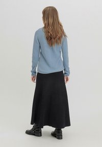 Top de manga larga de rayas azul claro, combinado con una falda maxi de rayas negra y botas negras hasta el tobillo, visto desde la parte de atrás.