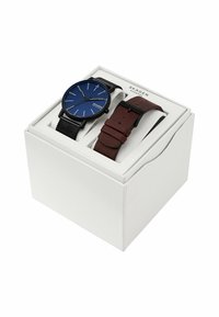 Le set de montres Skagen comprend un cadran bleu avec des index horaires blancs, un bracelet en maille noire et un bracelet en cuir marron, le tout emballé dans une boîte blanche.