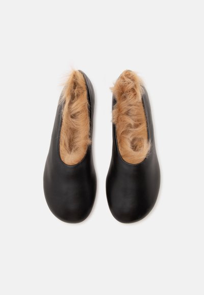 Paire de chaussures noires sans lacets avec une doublure en fourrure marron clair et duveteuse à l'intérieur, vue de dessus sur un fond blanc.