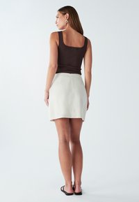 Rjava majica brez rokavov s kvadratnim izrezom in dvema gumboma na hrbtu, v kombinaciji s smetanasto mini krilo z bočnim zadrgo in gladko površino.