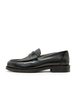 Mocasines de cuero negro con un acento de cuero negro texturizado, punta redondeada y un tacón bajo en bloque; presenta un detalle metálico decorativo.