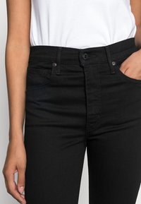 Jeans de tiro alto negros con una silueta ajustada, fabricados en denim, que cuentan con bolsillos delanteros y un cierre de botón con herrajes metálicos.