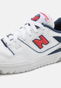 Sneaker bianca con accenti blu navy, logo "N" rosso, texture perforata e suola imbottita con il marchio "new balance". Numero di stile 550.