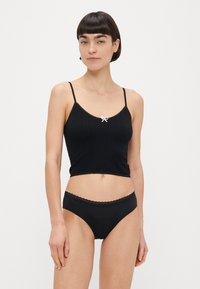 Camisole noire en maille avec bretelles ajustables, bordure en dentelle et petit nœud rose au centre devant, assortie à une culotte noire.