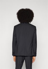 Black suit jacket made of smooth fabric, featuring a single vent, tailored fit, and buttoned cuffs. View from the back, no additional details.
