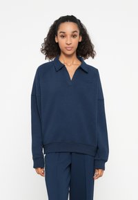 Navyblauwe sweatshirt met een polokraag, raglanmouwen en geribbelde manchetten. Voorzien van een geborduurd logo op de borst en een ontspannen pasvorm.