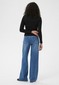 Plata kāju zilas denim bikses ar augstu jostasvietu, piecām kabatām un izbalējušu mazgāšanu, papildinātas ar pieguļošu melnu garām piedurknēm kreklu.