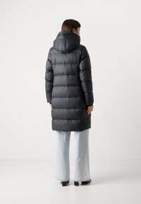Abrigo puffer negro con capucha, con un diseño acolchado y mangas largas. Lleva puesto sobre unos jeans de pierna ancha azul claro y botas negras hasta el tobillo.