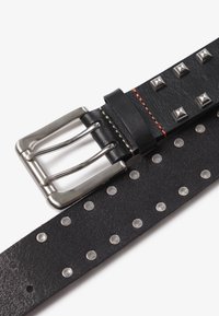 Sort læderbælte med sølvnitter og en metalspænde med dobbelt-prong design. Inkluderer en kontrasterende rød syning.