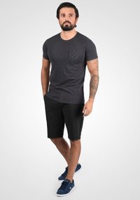 T-shirt gris foncé avec une poche à motif, accompagné de shorts noirs et de baskets navy. Le tissu semble doux et respirant.