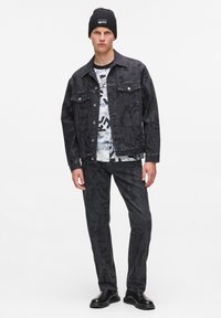 Jachetă din denim negru asociată cu un tricou grafic alb-negru și pantaloni din denim asortați. Țesătură texturată, design ajustat și cizme negre.