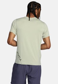 Maglietta sportiva a maniche corte verde chiaro con collo a giro. Presenta il logo nero "RVCA" nella parte bassa del retro sinistro. Tessuto morbido, vestibilità rilassata.