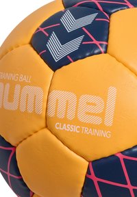 Træningsbold med orange og marineblå segmenter. Har et pink gittermønster, struktureret overflade og hvid branding "Hummel Classic Training."