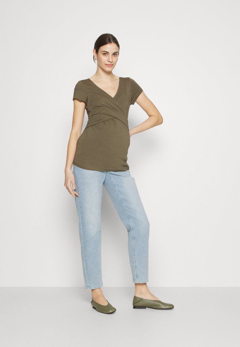 Oliven grønn omslagstopp med korte ermer, v-hals og samlet sidesøm. Kombinert med lyseblå straight-leg jeans og oliven grønne leiligheter.
