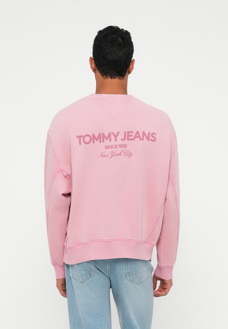 Rozā kokvilnas sporta krekls ar apaļu kakla izgriezumu, ribām pie piedurknēm un apakšmalas. Aizmugurē atrodas "TOMMY JEANS" logo, teksts "SINCE 1985" un "New York City".