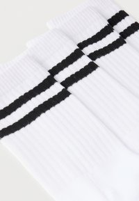 Hvide atletiksokker med ribbet tekstur, der har to sorte vandrette striber rundt om den øverste del. Blødt bomulds materiale.