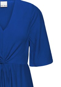 Robe bleu col en V avec manches courtes et détail de nœud torsadé à la taille, tissu texturé, étiquette portant la mention "ICHI" à l'intérieur du col.