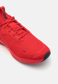 Rød atletisk sko med nett overdel, flate lisser og Polstret tunge. Har gummisåle med svarte detaljer og Puma-logo på siden.