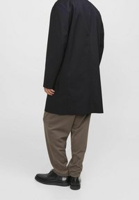 Black long coat with a smooth texture, paired with loose-fitting brown trousers. Black shoes complete the outfit.