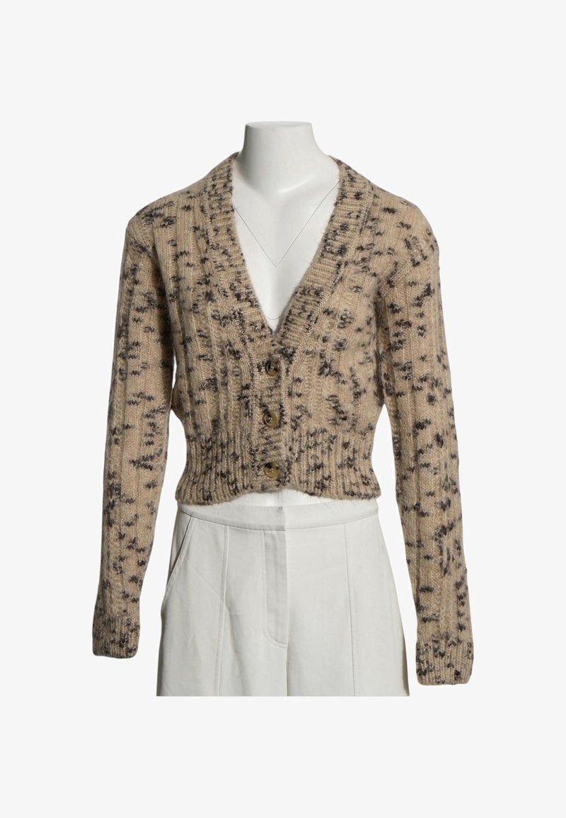 Cardigan en maille beige court avec un motif tacheté foncé, trois boutons et manches longues, porté sur un pantalon blanc taille haute.