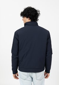 Marineblaue, Reißverschlussjacke mit Stehkragen, strukturiertem Stoff und seitlichen Taschen. Slim Fit, gerippte Bündchen und Saum.