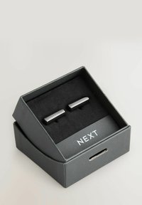 Silver cufflinks in a black gift box with soft black lining; sleek rectangular design with polished surface, featuring the brand name "NEXT."