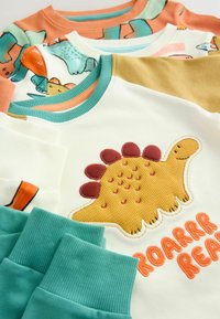 Vier Sweatshirts in verschiedenen Farben: Weiß mit einem gelben Dinosaurier-Graphic, türkisfarbene Bündchen sowie orangefarbene, grüne und braune Akzente. Weicher Stoff.