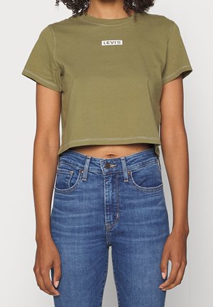 Personne portant un t-shirt court Levi's vert olive et un jean en denim bleu taille haute, debout avec les bras détendus le long du corps.