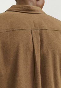 Brown woolen shirt with a straight collar, featuring a center seam down the back and a soft, textured fabric.