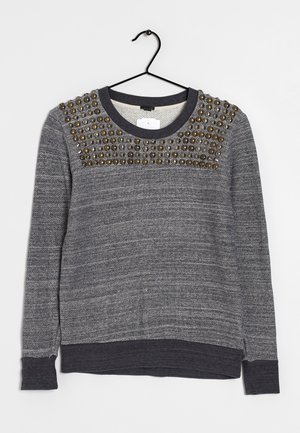 Pull gris avec un tissu texturé, présentant un col rond et des clous décoratifs sur les épaules. Manches longues et poignets côtelés.