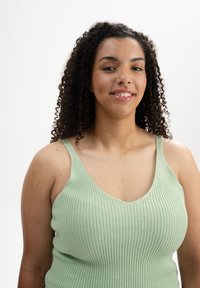 Helles grünes, geripptes Tanktop mit tiefem V-Ausschnitt und dünnen Trägern, das eine weiche Textur und eine figurnahe Passform zeigt.