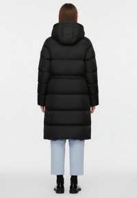 Sort polstret frakke med hætte, der har en indsnævret talje og en længde til knæene. Glat stofftekstur, vandrette syede sektioner, minimalistisk design.