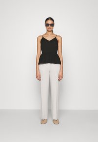Svart peplum-top med tynne stropper, kombinert med lysegrå vide bukser. Eyewear har et moderne vinkelrett design. Teksturert beige sko.