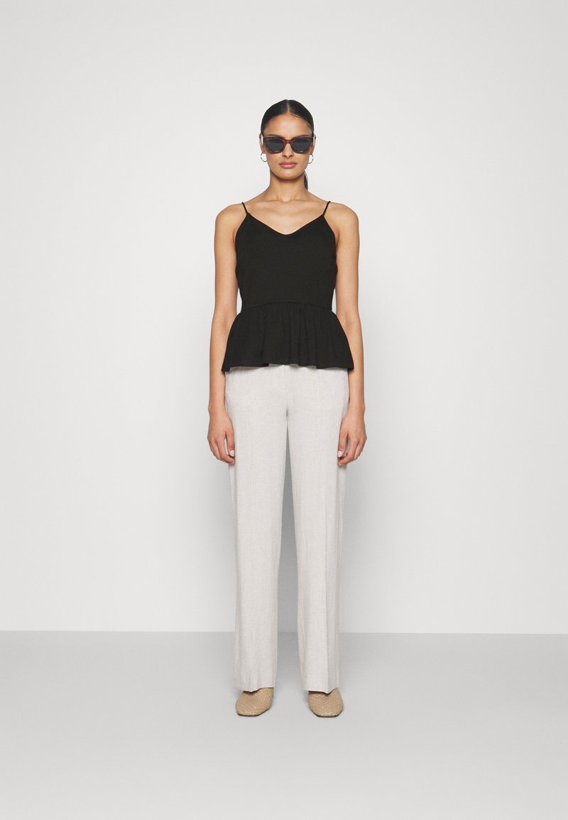 Svart peplum-top med tynne stropper, kombinert med lysegrå vide bukser. Eyewear har et moderne vinkelrett design. Teksturert beige sko.